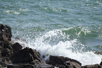 The sea wave crashing on the rock. Waves splashing on rocks in the sea on a sunny day.