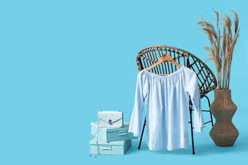 Hanger with stylish female blouse hanging on armchair, handbag, boxes and pampas grass against...