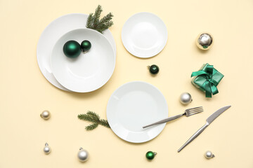 Beautiful table setting with Christmas balls, gift box and fir branches on yellow background