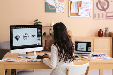 Young female graphic designer working with computer and color palettes at table in office
