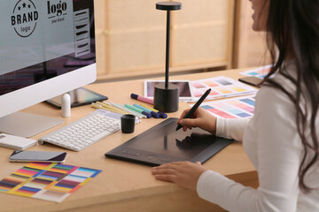 Young female graphic designer working with tablet at table in office, closeup