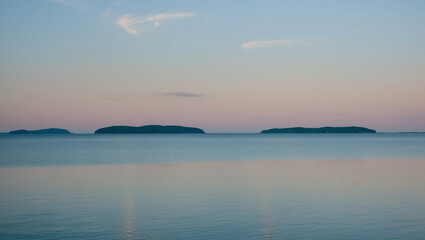 Obraz premium Tranquil Lake Under a Pastel Morning Sky with Distant Islands on the Horizon