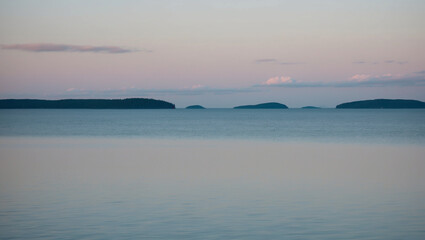Obraz premium Tranquil Lake Under a Pastel Morning Sky with Distant Islands on the Horizon