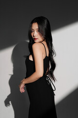 光と影の背景で撮影をした黒いドレスを着た若い女性のシックなポートレート