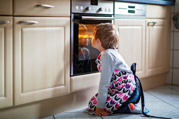 Cute blond boy baking muffins or pie in domestic kitchen. Happy child having fun with helping,...