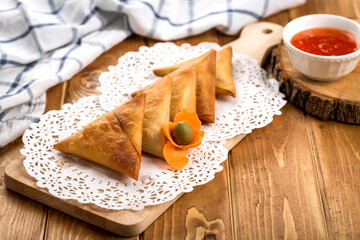 Samosa or Samboosa filled with vegetable and meat isolated on wooden board with tomato sauce on table side view of arabic ramadan food