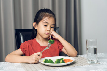 Little cute kid girl refusing to eat healthy vegetables. Children do not like to eat vegetables.