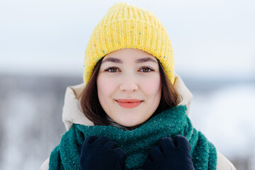 young beautiful slim asian girl standing outdoors in winter day smiling to camera, dressed in knitted yellow cap and green scarf, winter portrait