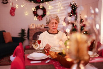Loneliness, loneliness during Christmas holidays. Senior woman sitting at dining table near decorated Christmas tree at home. Lonely senior woman celebrating Christmas alone.