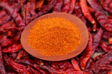 Dried chilies or Capsicum annuum L, piled up and on top there is a wooden bowl containing ground chilies. With a close look.
