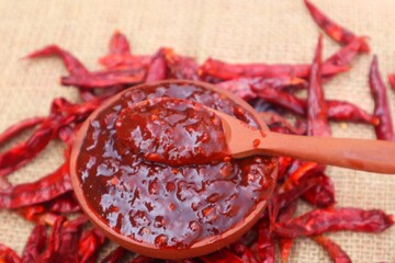 Terasi chili sauce in a wooden bowl and surrounded by dried chilies piled up around it. With a...