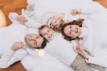 Laughing family with two children lies on a white fluffy carpet