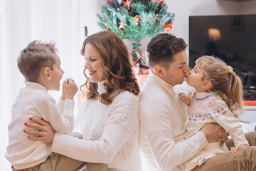 A happy family with two children in knitted sweaters sits near tree