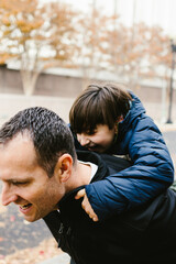 Dad gives son piggyback ride with fall trees in urban area