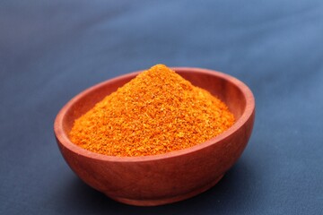 Wooden bowl containing dried chili powder or Capsicum annuum L, isolated on a dark background. With a close look.