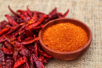 Chili powder in a wooden bowl and dried chilies or Capsicum annuum L, piled on the side. With a close look.