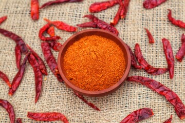 Chili powder in a wooden bowl and dried chilies or Capsicum annuum L, scattered around it. With a close look.
