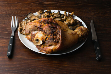 Pork shank baked in beer with mushrooms on a dark background. A delicious restaurant dish on a plate