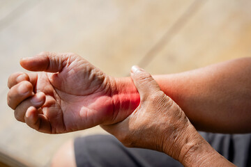 elderly person gently holds their wrist, possibly experiencing pain or discomfort, in close up...