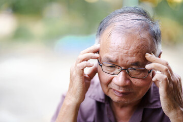 Feeling overwhelmed, elderly man with glasses holds his head in distress, reflecting moment of deep...