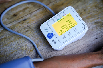 digital blood pressure monitor displaying systolic and diastolic readings on wooden surface,...