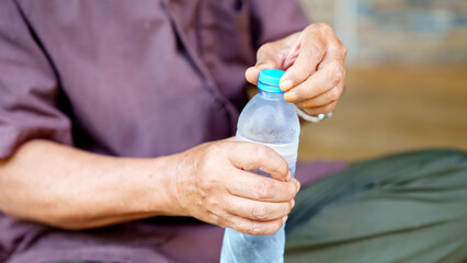 person holding cold water bottle, twisting cap open with both hands, suggesting refreshment and hydration. focus is on hands and bottle, with blurred background