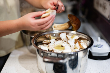 A person cleans and chops fresh mushrooms, placing them into a pot in a modern kitchen setting, emphasizing home cooking and culinary preparation.