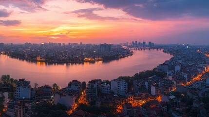 Obraz premium A panoramic view of Hanoi's skyline at sunset, with the Red River and bridges illuminated by