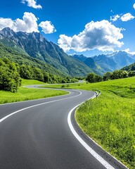 Naklejka premium A scenic winding road through lush green fields, framed by majestic mountains and a vibrant blue sky, perfect for travel photography.