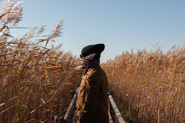 Sideview of a man standing on a bridge surrounded by reed thickets