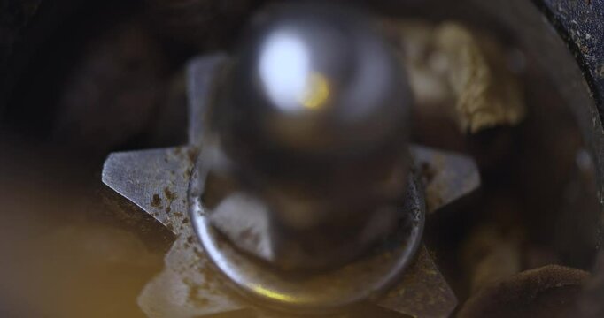 Slow motion, macro shot inside of a conical burr coffee grinder that keeps getting stuck while grinding coffee beans