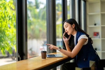 A woman is talking on her cell phone while pointing to something on her laptop