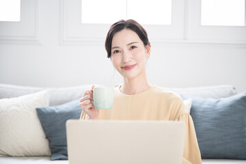 コーヒーやお茶を飲みながらパソコンの作業をする日本人(アジア人)女性　コピースペースありのカメラ目線