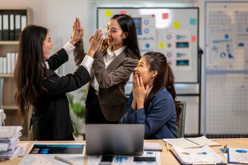 Three women in business attire are high fiving each other in a conference room