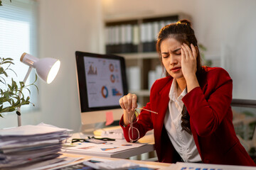 A woman in a red jacket is sitting at a desk with a computer monitor