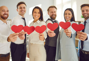 Group of business people stands in the office, holding red hearts. Love and togetherness, possibly...