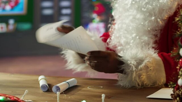 African american Saint Nick opening letters from children in his festive workshop, man in red suit and white beard checking mailbox. Surrounded by holiday lights, Santa prepares gifts. Camera A.