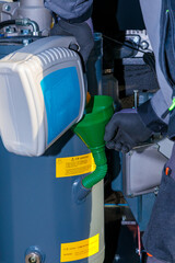 Close-up of a technician pouring oil into an industrial compressor using a funnel, performing...