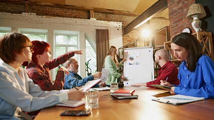 Multigenerational team collaborates on project, exchanging ideas in relaxed, productive office atmosphere. Teamwork across generations. Concept of office, teamwork, teaching, working. Ad.