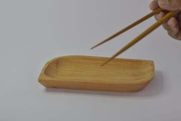 close up of wooden plate with chopsticks held by adult hand, isolated on white background