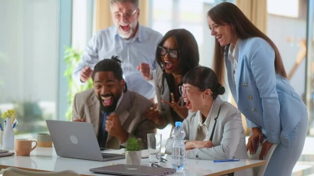 Cheerful multiracial team looking at laptop receiving important email message with positive feedback, employees looking forward celebrating good results and achievement at work applauding and dancing 