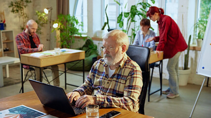 Senior man, leader sitting at desk with laptop, working in modern co-working space. Success...