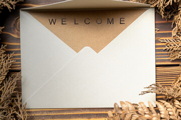 Top view of envelope and postcard with brown card with words Welcome on it and wreath. Greeting for...