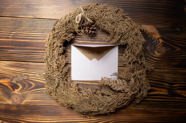 Top view of envelope and postcard with brown card with words Thank You written on it and wreath