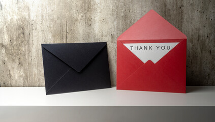 Red envelope and postcard with white card with words Thank You written on it on the shelf wall