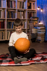 Fototapeta premium A young boy sitting with pumpkins in a cozy room, surrounded by books. Ideal for autumn, harvest, and Thanksgiving themes, showcasing warmth and the beauty of fall traditions.