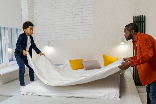 Father and son making bed in the morning together - Powered by Adobe