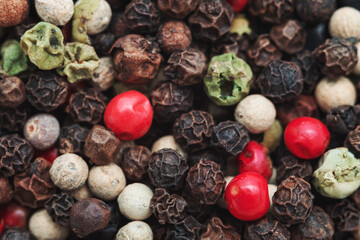 A close-up of a mix of colorful peppercorns, including black, white, green, and red varieties. The different textures and colors of the peppercorns create a rich, vibrant pattern.