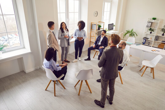 Team and coach talking, active multiracial group of office workers brainstorming, discussing business strategy, ideas, team building activity, professional conversation during meeting conference