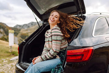 Young woman sits in the trunk of a car. Autumn landscape. The concept of traveling by car, active...